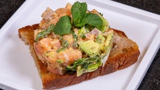 Rezept für Lachstatar mit Avocado: Das fertige Gericht ist auf geröstetem Brot angerichtet.