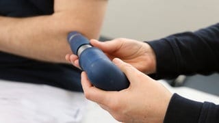 Ein Orthopäde richtet eine Sonde zur Behandlung mit Stoßwellen auf den Ellenbogen eines Patienten