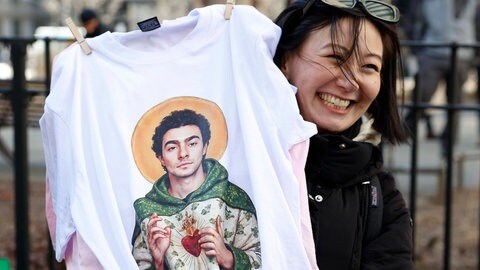 Frau hält T-Shirt mit Luigi Mangione als Heiliger hoch
