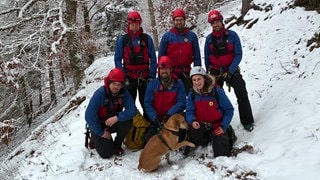Bergwacht rettet Hund Leo - fünf Männer und eine Frau in Bergwachtausrüstung machen ein Gruppenfoto mit dem Hund. Es liegt Schnee.