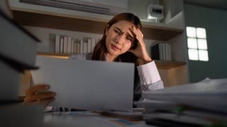 Spätabendlicher Stress. Junge Frau fühlt sich bei der Durchsicht von Dokumenten überfordert.