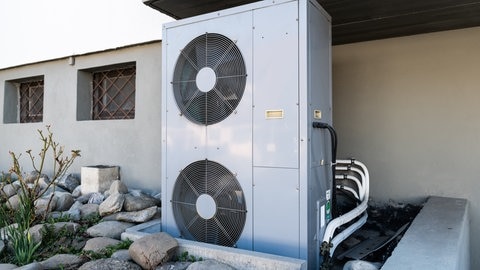 Die Lüftungsanlage einer Wärmepumpe steht vor einem Wohnhaus.