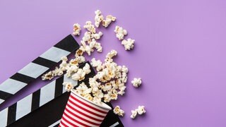 Eine Filmklappe und Popcorn auf violettem Grund.