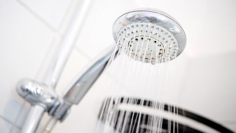 Ein Duschkopf hängt in einer Dusche in einem Badezimmer. Auch beim Duschen lässt sich Wasser sparen.