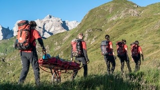 Bergretterinnen und Bergretter aus Vorarlberg laufen mit einer Gebirgstrage zu einem Einsatz.