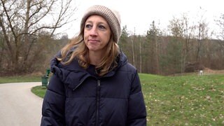 Eine Frau steht mit Mütze und Wintejacke auf einem Feldweg.