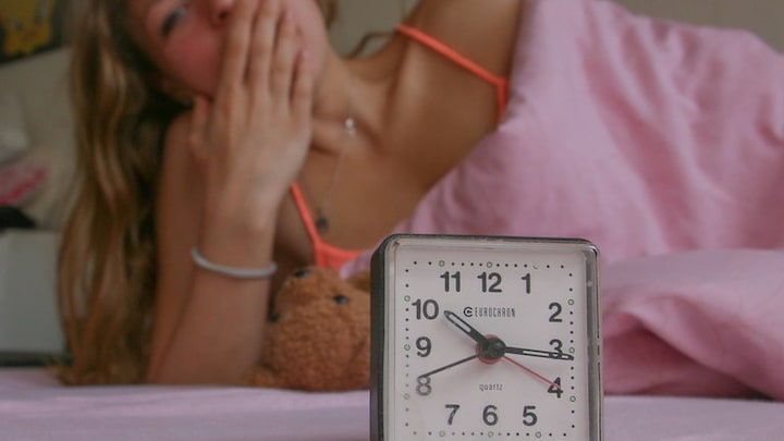 Frau mit Wecker, unausgeschlafen. Unsere innere Uhr folgt der Sonne - Winterzeit passt besser zu unserem natürlichen Schlaf- und Aufstehrhythmus.