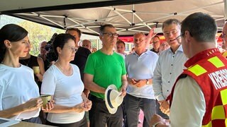 Ministerpräsident Cem Özdemir (Grüne) und Landeswirtschaftsministerin Marion Gentges (CDU) sprechen beim Besuch in Zell am Harmersbach (Ortenaukreis) mit Einsatzkräften der Feuerwehr. Sie stehen dabei in eienem Zelt. Özdemir bedankte sich für den Einsatz der ehrenamtlichen und hauptamtlichen Helferinnen und Helfer.