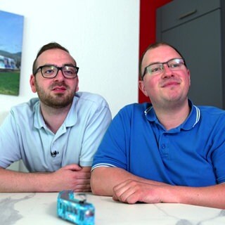 Die beiden Straßenbahnfahrer Marco und Daniel Rungenhagen sitzen in ihrer Küche. Vor ihnen auf dem Tisch steht eine blaue Modell-Straßenbahn.