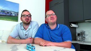 Die beiden Straßenbahnfahrer Marco und Daniel Rungenhagen sitzen in ihrer Küche. Vor ihnen auf dem Tisch steht eine blaue Modell-Straßenbahn.