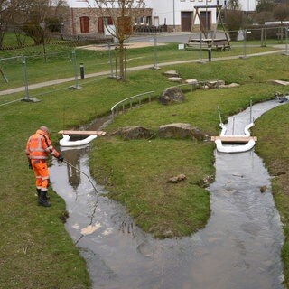 Mit einer Ölsperre pumpen Arbeiter mit Diesel kontaminiertes Oberflächenwasser aus einem Bach ab, der in der in Kisselbach an einem Spielplatz vorbeifließt