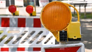 Eine orangene Warnleuchte auf einem rot-weißen Absperrzaun. Zwei Brücken in Speyer müssen wegen Brückenschäden vom Landesbetrieb für Mobilität gesperrt werden. Das wird für Probleme im Stadtverkehr sorgen.