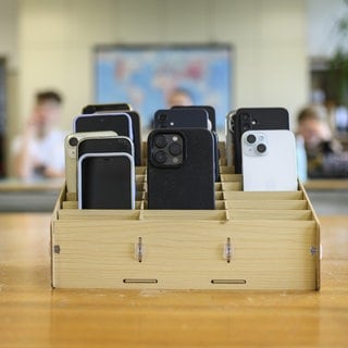 Mobiltelefone einer Schulklasse, vor Unterrichtsbeginn mit der "Handygarage" eingesammelt, kommen sie in einen Schrank.