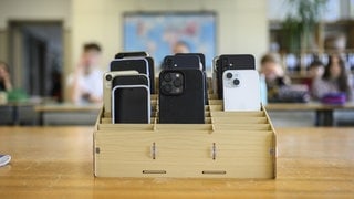 Mobiltelefone einer Schulklasse, vor Unterrichtsbeginn mit der "Handygarage" eingesammelt, kommen sie in einen Schrank.