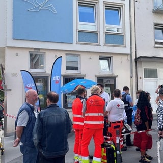 Mehrere Rettungskräfte und Polizisten stehen um einen Stand der AfD herum. Auf den Stand wurde eine Flüssigkeit geschüttet.