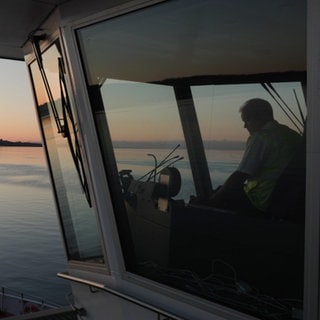 Eine Fähre steht auf dem Bodensee, auf der linken Seite sieht man den Sonnenaufgang.