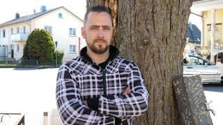Mann steht mit verschränkten Armen an Baum angelehnt