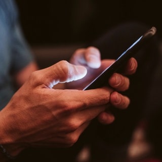 Mann hält ein Handy. Die Nutzung von Smartphones wird kontrovers diskutiert und unterschiedlich gehandhabt.