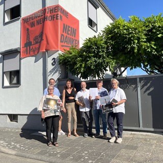 Menschen stehen vor einem roten Plakat, darauf steht: Tiefengeothermie in Neuhofen - Nein Danke!