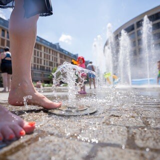 Eine Frau kühlt ihre Füße an Wasserfontänen.