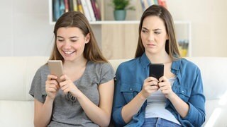 Eine Frau schaut neidisch auf das Handy der Frau neben ihr