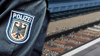 (Montage) Ein Abzeichen der Polizei auf einem Jackenärmel. Im Hintergrund ein Gleisbett. Eine Jugendliche hat sich in Wannweil auf ein Gleisbett gelegt und ist anschließend lachend davongerannt 
