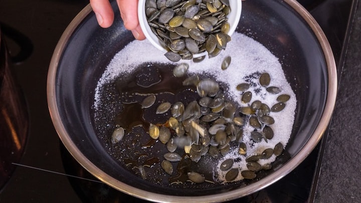 Es werden Kürbiskerne in die Pfanne gegeben. In der Pfanne befindet sich bereits geschmolzene Butter.