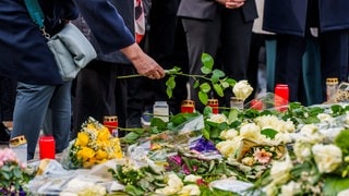 Menschen legen Blumen und Kerzen nieder.