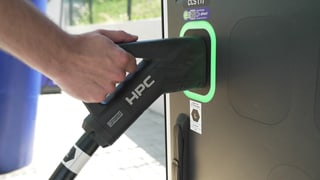 Ein Mann steckt das Kabel eines E-Autos in eine Schnellladesäule.