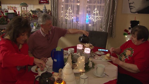 Zwei Frauen und ein Mann sitzen an einem weihnachtlich geschmückten Tisch und essen Zimtschnecken. 