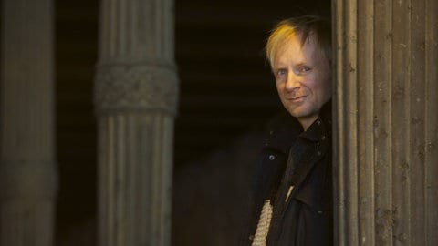 Der Schrifsteller Jochen Schmidt im Halbdunkel an eine Steinsäule gelehnt.
