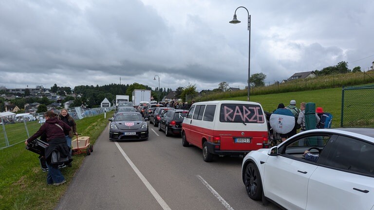 Fahrzeuge stehen in Schlange, die Fans für Rock am Ring laufen entlang der Straßen von Nürburg.