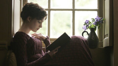  Anne Hathaway sitzt als Jane Austen am Fenster, ließt ein Buch