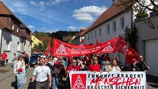 Menschen mit roten Plakaten der IG Metall ziehen durch Münsingen. Der Maschinenherstellers Walter will Stellen streichen.