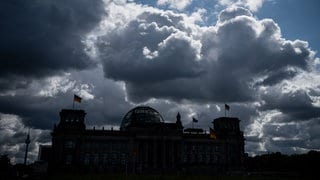 Die Sonne versteckt sich hinter dunklen Wolken über dem Reichstag, dem Sitz des Deutschen Bundestags.