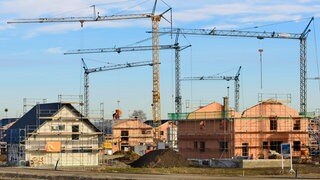 In einem Neubaugebiet stehen viele Baukräne vor Wohnhäusern im Rohbau, als Symbolbild für Wohnbau und Wohnungspolitik