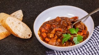 Das Gulasch aus Ungarn wird in einem weißen Teller mit zwei Baguettscheiben präsentiert. Das Rezept für das Gulasch ist einfach nachzukochen.