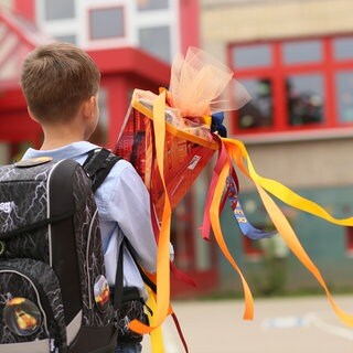 Ein Junge steht mit seiner Schultüte vor einem Schulgebäude.