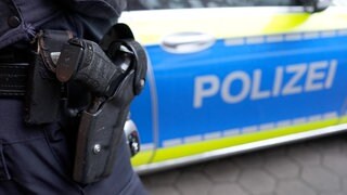 Ein Polizist steht vor einem Einsatzfahrzeug der Polizei (Symbolbild).