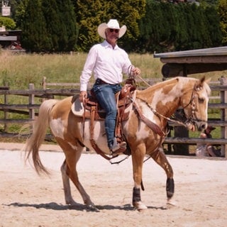 Mann im Cowboy-Outfit sitzt auf einem Pferd