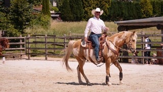Mann im Cowboy-Outfit sitzt auf einem Pferd