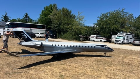 EIn Mann sthet neben einem originalgetreu nachgebauten Jet. DIe Miniatur-Flugzeugmodelle sind mehrere Meter lang. 