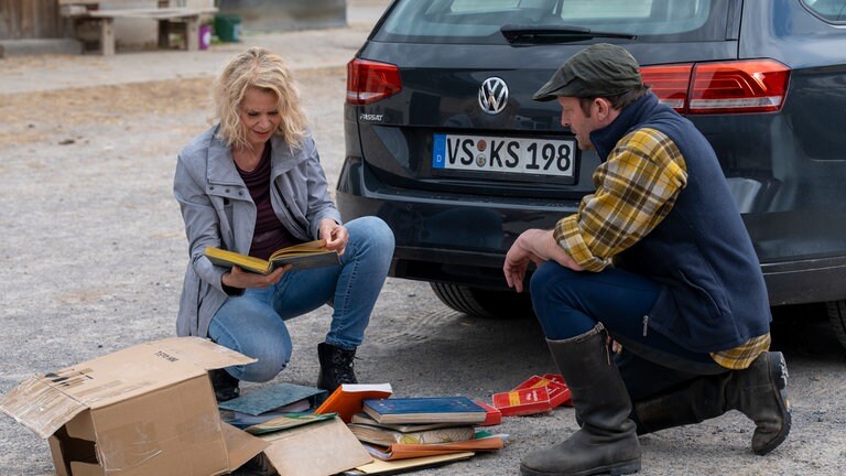 Kati und Bernd knien vor dem Inhalt eines aufgeplatzten Umzugskartons