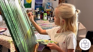 Milia steht vor ihrer Leinwand und malt. Die 8-Jährige hat eine Palette mit Farben und einen Pinsel in der Hand. Im Hintergrund hängen Bilder an der Wand. Milia macht ihre eigene Kunst·ausstellung. Rechts das SWR Logo für Leichte Sprache.