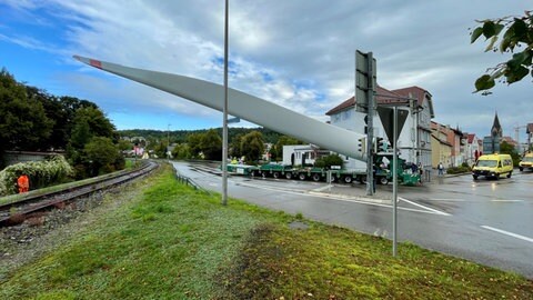 Ein Rotorblatt für einen Windpark im Kreis Reutlingen wird bei einem Schwertransport auf die Alb gebracht. Es muss in einem Ort um eine enge Kurve manövriert werden und ragt weit über die Straßenränder hinaus.