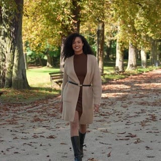 Junge Frau in herbstlichem Outfit: Strickkleid und Cardigan mit Stiefeln und Gürtel