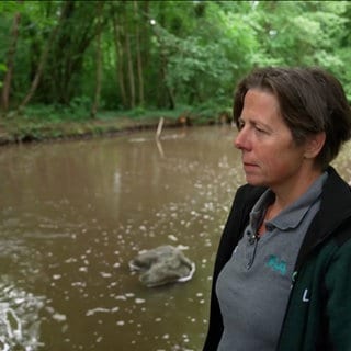 Eine Frau steht neben einem kleinen See zwischen Bäumen