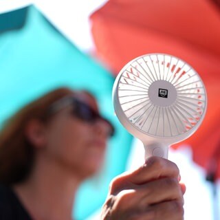 Eine Frau kühlt sich mit einem Handventilator ab (Symbolbild). RLP leidet unter einer Hitzwelle.
