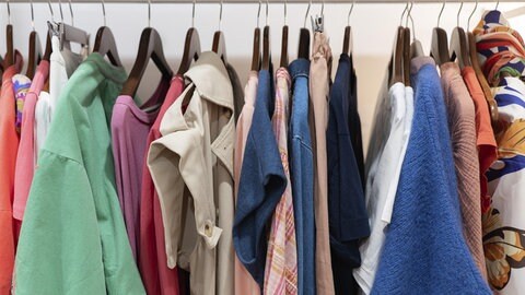 Ein Schrank mit unterschiedlichen Kleidungsstücken, die auf Bügeln aufgehängt sind.