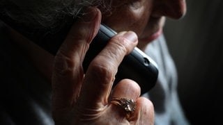 Ältere Frau telefoniert mit einem Smartphone und trägt Ringe an der Hand. Symbolbild für Betrug durch "falsche Polizisten" am Telefon.